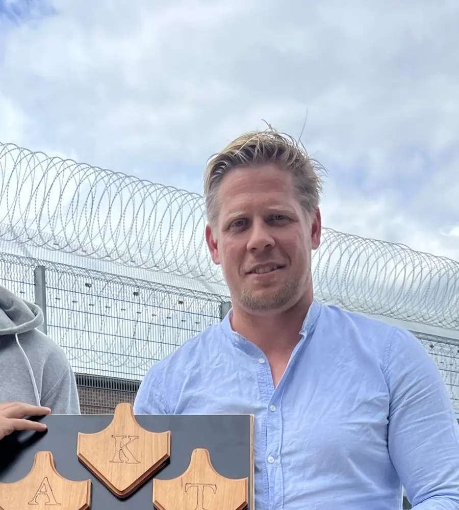 Steffen Knippertz vor einem Sicherheitszaun, im Vordergrund ein Holzschild mit den Buchstaben A, K und T